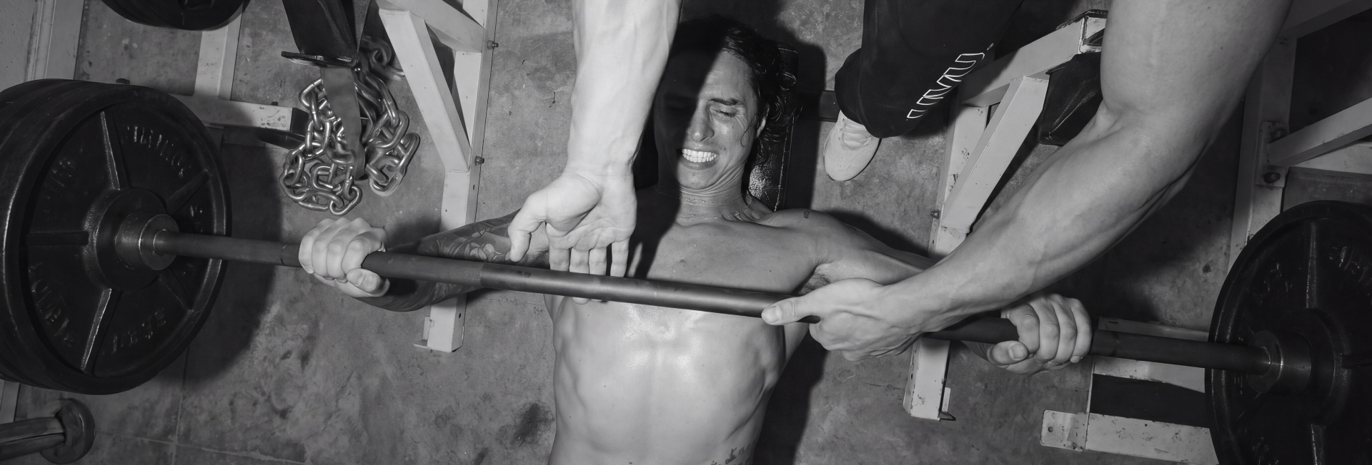 Athlete training under a loaded barbell with a spotter